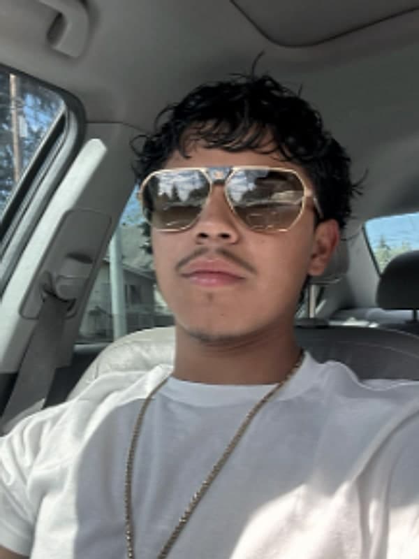 Person in aviator sunglasses wearing a white tee and gold chain