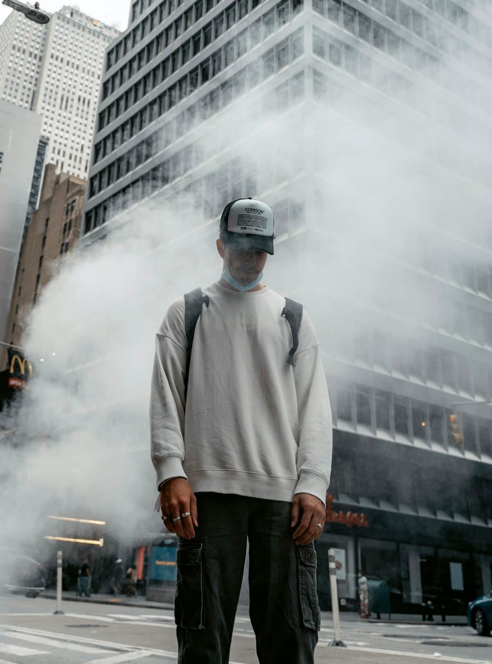 Man in a grey sweatshirt and cap standing in city steam