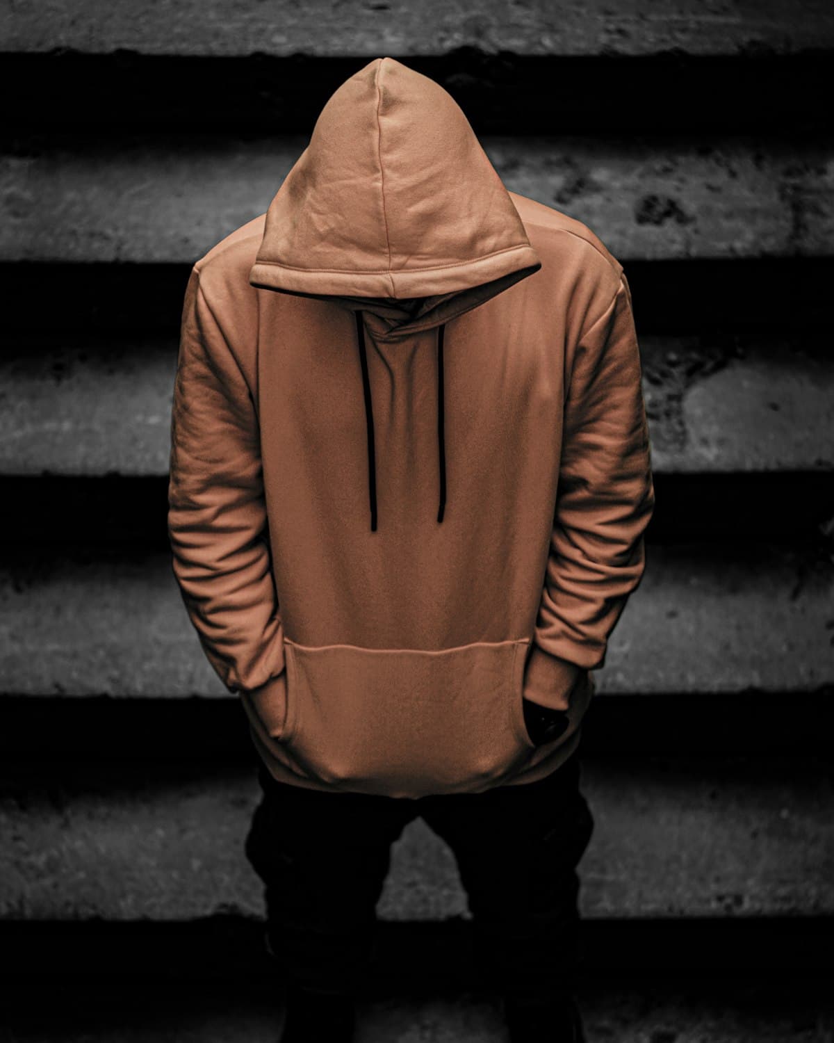 Hooded figure in a rust-coloured oversized hoodie on dark stairs