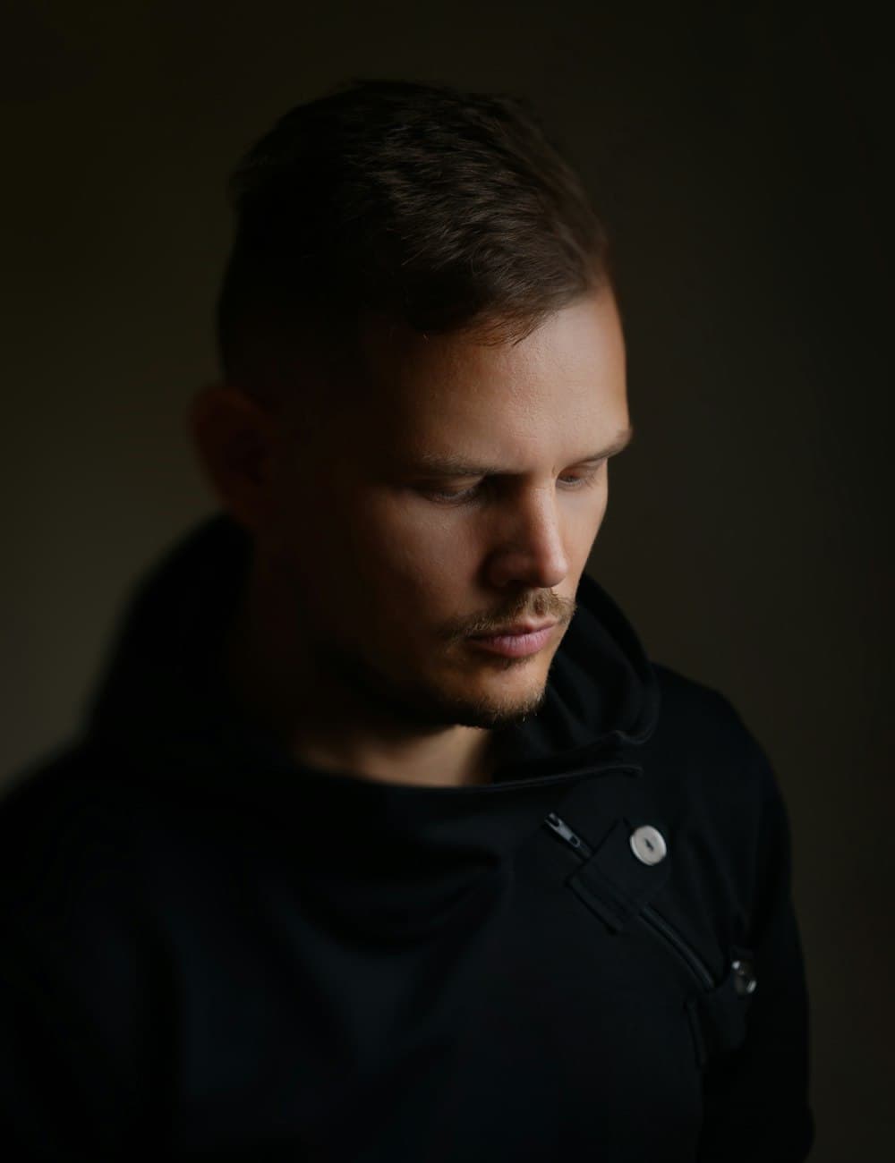 Man in a black high-neck layer against a dark backdrop